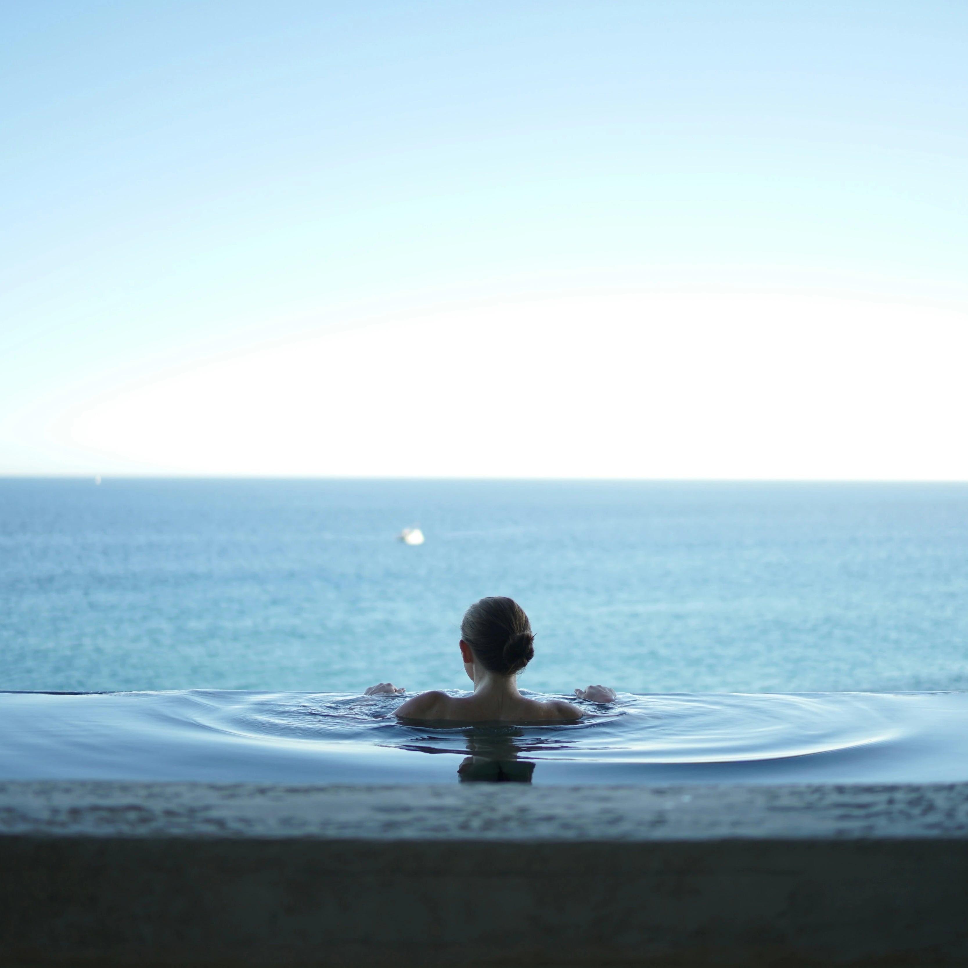 Femme dans une piscine à débordement face à la mer, détente, bien-être