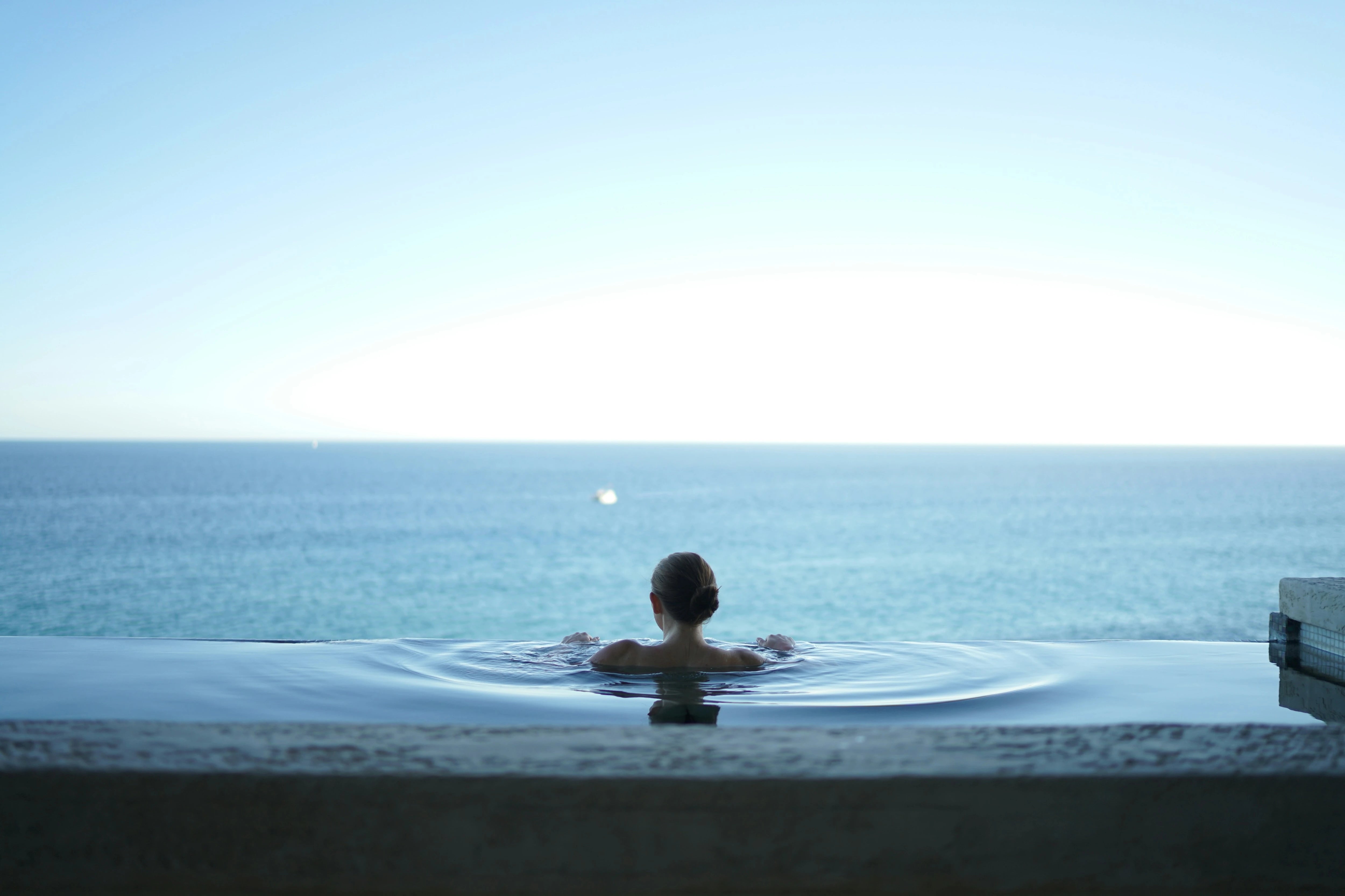 Femme dans une piscine à débordement face à la mer, détente, bien-être